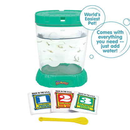 A teal aquarium is filled with water and Sea-Monkeys. Laying in front, there are three packets, numbered 1, 2, and 3 from left to right. There is a small yellow Sea-Monkeys spoon laying in front of the packets. There are two callouts in circles. One reads "World's Easiest Pet!" and the other reads "Comes with everything you need - just add water!"