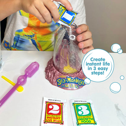 A child wearing a white shirt with bright colors printed on it is holding the Magiquarium with one hand, and pouring powder from a small packet labled with the number 1 with the other hand. A packet with the number 2, a packet with the number 3, a purple pipette, and a yellow plastic spoon all lay on the surface in front of the child. There is a callout in a circle that reads "Create instant life in 3 easy steps!".